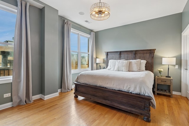 bedroom with light wood-type flooring, visible vents, a notable chandelier, and baseboards