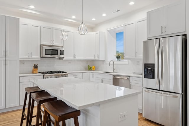 kitchen with visible vents, light wood-style flooring, a center island, light stone countertops, and stainless steel appliances