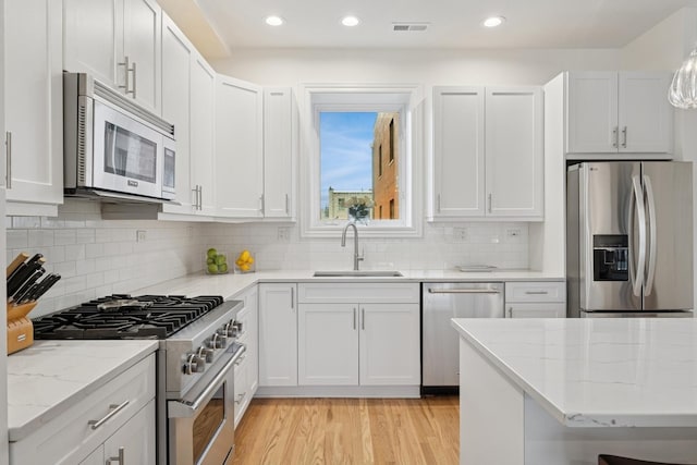 kitchen with light wood-style flooring, a sink, visible vents, appliances with stainless steel finishes, and light stone countertops