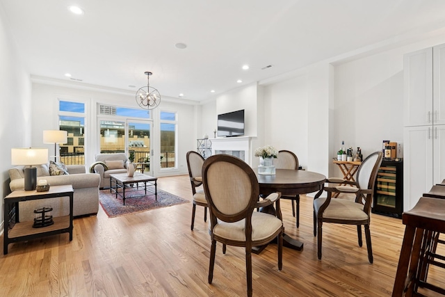 dining space featuring light wood-style flooring, wine cooler, a fireplace, a notable chandelier, and recessed lighting