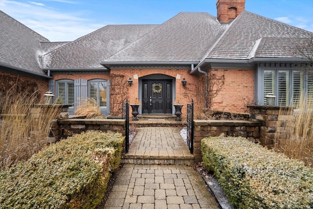 view of front facade with roof with shingles, a chimney, and brick siding