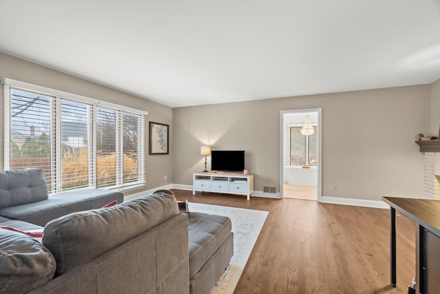 living room featuring visible vents, a fireplace, baseboards, and wood finished floors