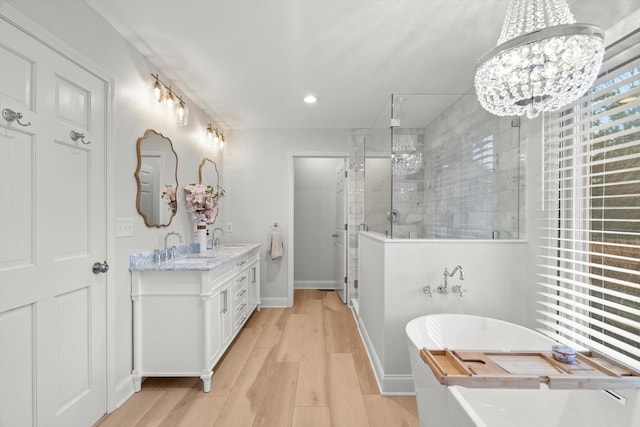 bathroom with a sink, wood finished floors, a soaking tub, a stall shower, and an inviting chandelier