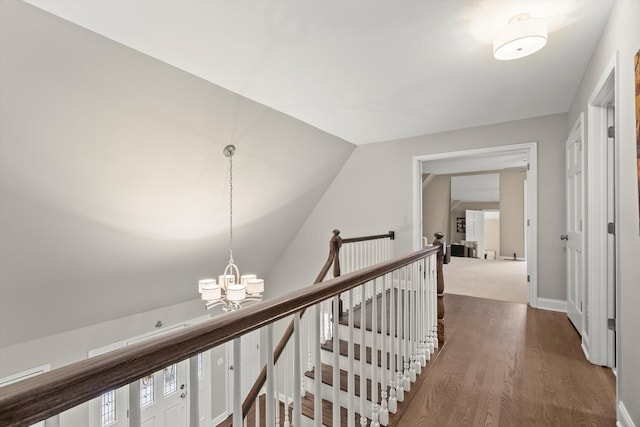 corridor with dark wood finished floors, vaulted ceiling, an upstairs landing, a chandelier, and baseboards