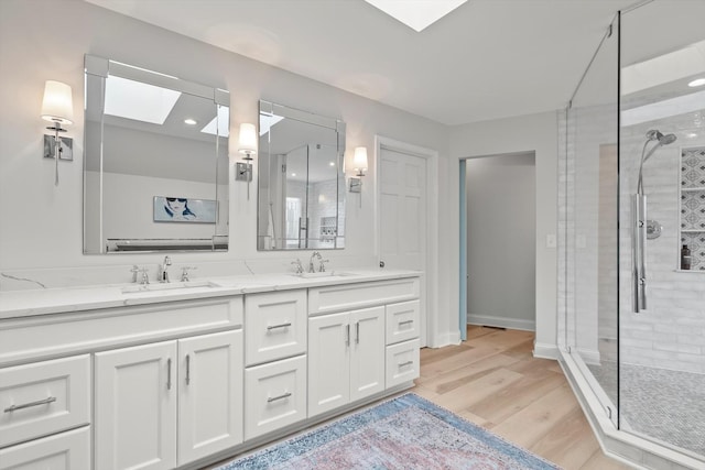 bathroom featuring wood finished floors, a stall shower, a skylight, and a sink