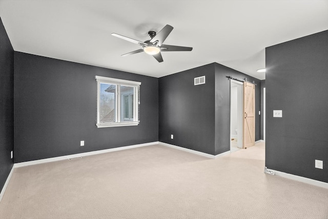 unfurnished room featuring a barn door, visible vents, baseboards, and a ceiling fan