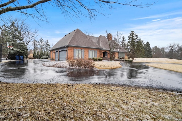 view of side of home featuring a garage, brick siding, driveway, and a chimney