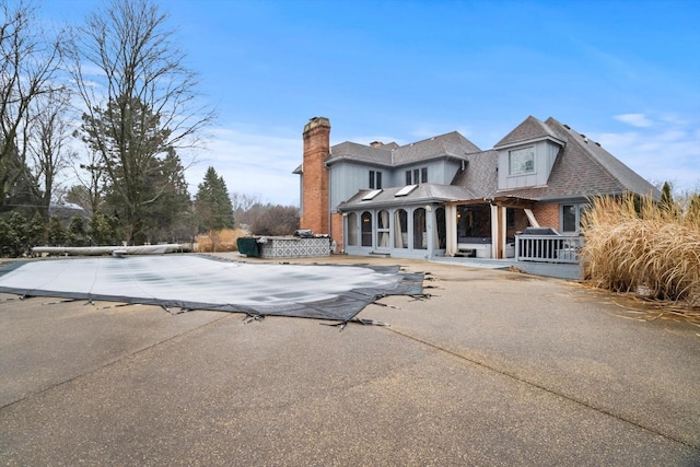 back of house with driveway, a patio area, a chimney, and brick siding