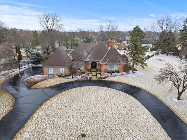 view of front of property featuring aphalt driveway, brick siding, a shingled roof, and a chimney