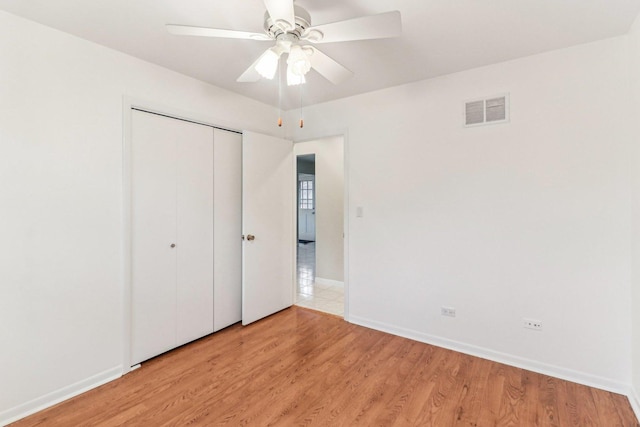 unfurnished bedroom featuring ceiling fan, visible vents, baseboards, a closet, and light wood finished floors