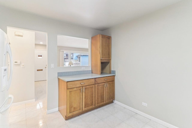 kitchen with light tile patterned floors, baseboards, light countertops, freestanding refrigerator, and brown cabinetry