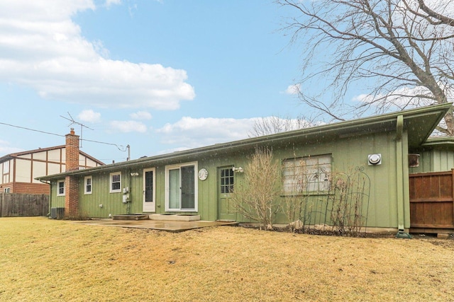 back of house featuring a yard, fence, a chimney, and central AC unit