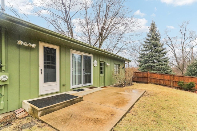 entrance to property featuring a patio, a lawn, fence, and board and batten siding