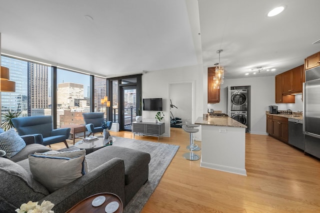 living area featuring baseboards, light wood-style floors, expansive windows, stacked washing maching and dryer, and recessed lighting