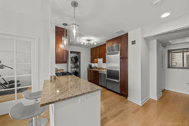 kitchen with stacked washer and dryer, light wood finished floors, a breakfast bar area, a peninsula, and stainless steel appliances