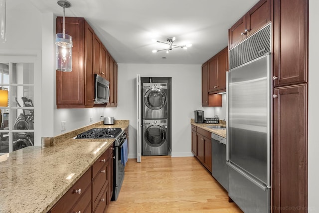 kitchen with baseboards, stacked washer / drying machine, light stone countertops, stainless steel appliances, and light wood-type flooring