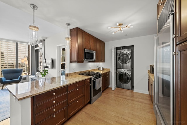 kitchen featuring a peninsula, appliances with stainless steel finishes, stacked washing maching and dryer, light wood finished floors, and plenty of natural light