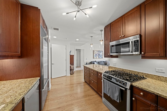 kitchen featuring light stone counters, pendant lighting, stainless steel appliances, visible vents, and light wood-type flooring