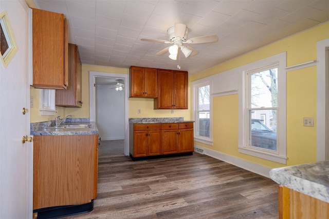 kitchen featuring dark wood-type flooring, brown cabinetry, a sink, and a ceiling fan