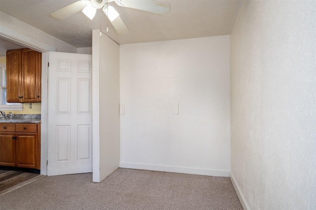 kitchen featuring brown cabinetry, a ceiling fan, carpet flooring, a sink, and baseboards