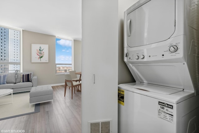 washroom with laundry area, visible vents, baseboards, light wood-style flooring, and stacked washer / drying machine