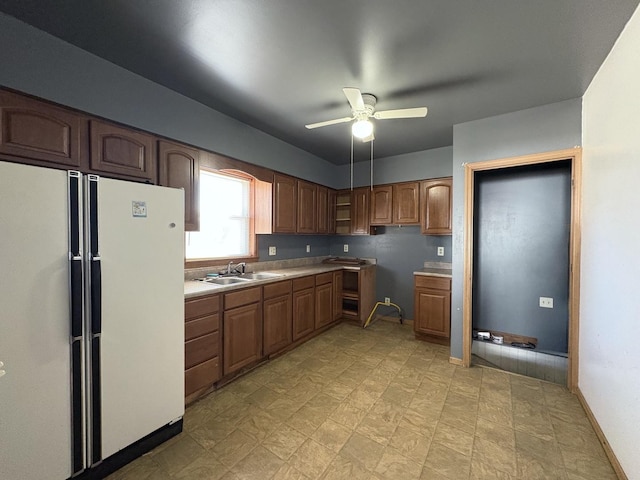 kitchen featuring a sink, freestanding refrigerator, brown cabinetry, light countertops, and baseboards