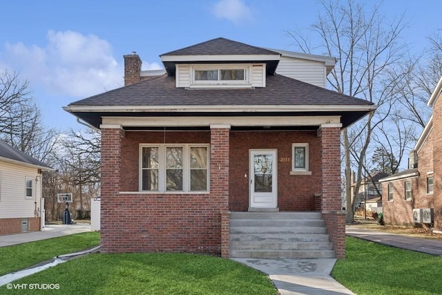 bungalow-style home featuring roof with shingles, brick siding, a front lawn, and a chimney