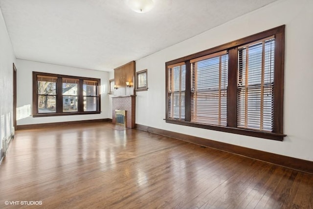 unfurnished living room with a brick fireplace, wood-type flooring, and baseboards