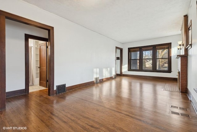 unfurnished living room featuring a brick fireplace, wood finished floors, visible vents, and baseboards