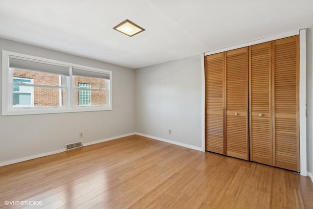 unfurnished bedroom with light wood finished floors, baseboards, visible vents, and a closet