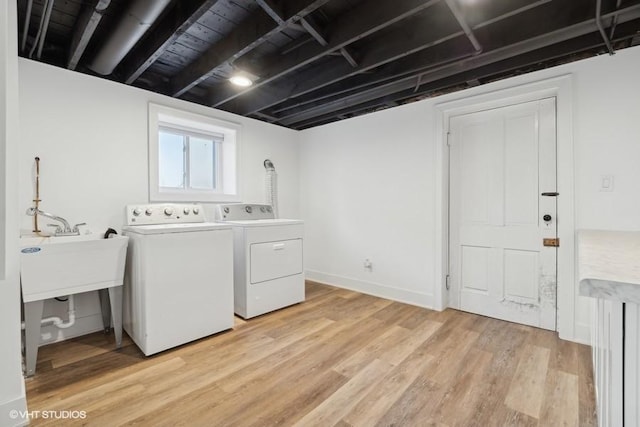 washroom featuring laundry area, light wood finished floors, baseboards, separate washer and dryer, and a sink