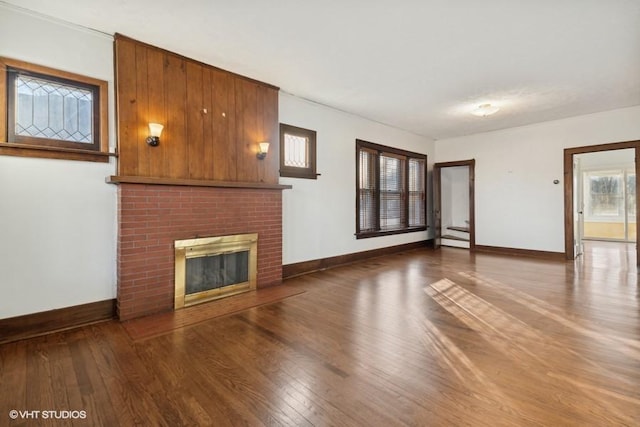 unfurnished living room with hardwood / wood-style floors, a brick fireplace, and baseboards