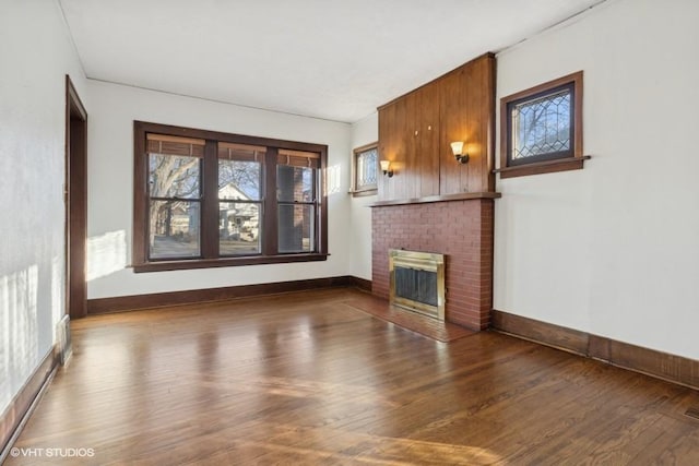 unfurnished living room featuring a brick fireplace, baseboards, and wood finished floors