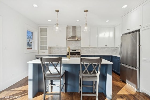 kitchen featuring light countertops, appliances with stainless steel finishes, white cabinetry, wall chimney range hood, and blue cabinets