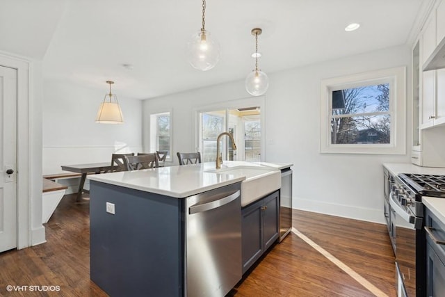 kitchen featuring dark wood-style floors, appliances with stainless steel finishes, hanging light fixtures, light countertops, and a sink