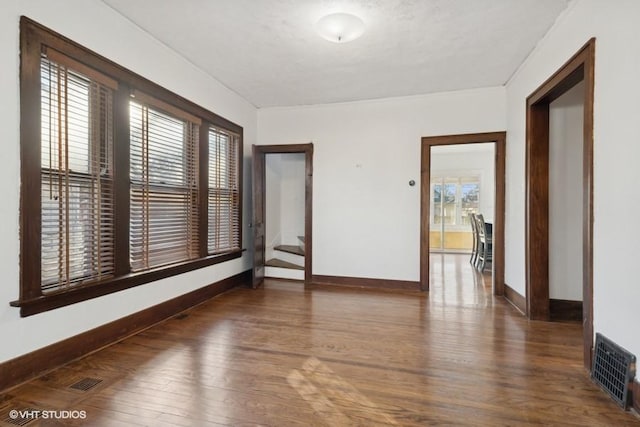 empty room featuring visible vents, plenty of natural light, baseboards, and wood finished floors