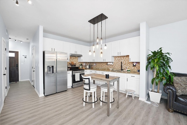 kitchen with appliances with stainless steel finishes, white cabinetry, under cabinet range hood, and tasteful backsplash