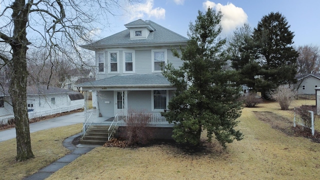 american foursquare style home featuring covered porch, roof with shingles, and a front yard