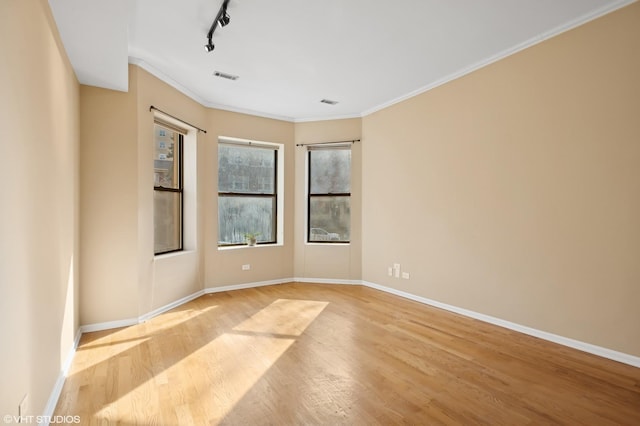 unfurnished room featuring crown molding, visible vents, track lighting, wood finished floors, and baseboards