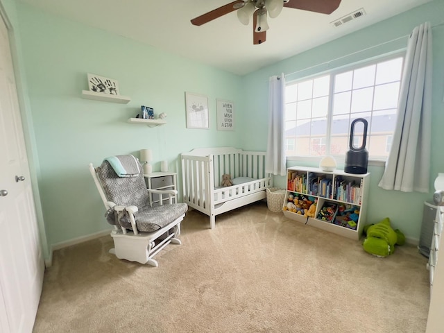 carpeted bedroom featuring a crib, a ceiling fan, visible vents, and baseboards