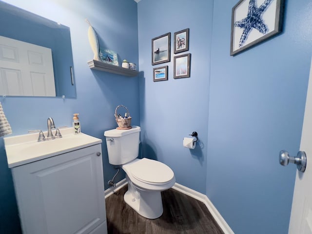 half bath with baseboards, toilet, wood finished floors, and vanity