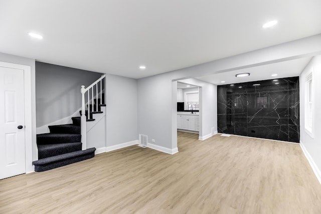 finished basement featuring stairs, light wood-type flooring, a sink, and baseboards