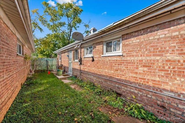 view of side of property featuring fence, a lawn, and brick siding