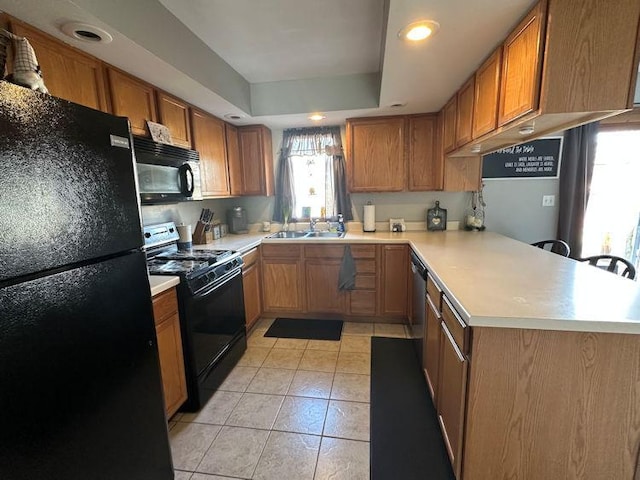 kitchen featuring a peninsula, light countertops, brown cabinets, black appliances, and a raised ceiling