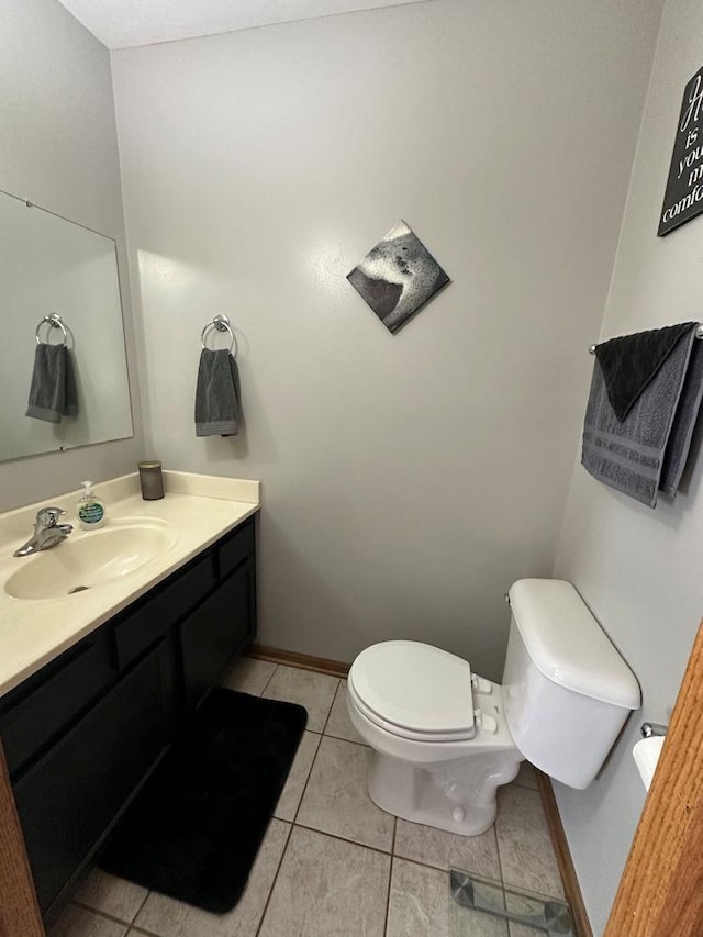 half bathroom with toilet, tile patterned flooring, baseboards, and vanity