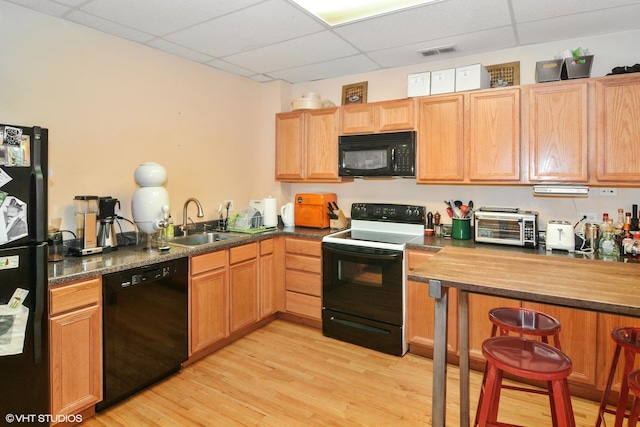 kitchen with a drop ceiling, a sink, light wood-type flooring, black appliances, and dark countertops