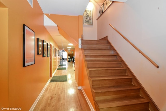 staircase with wood finished floors, visible vents, and baseboards