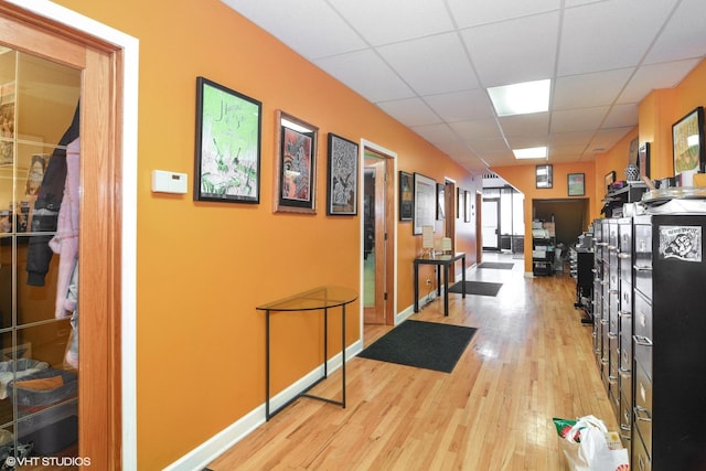 corridor featuring wood finished floors, a paneled ceiling, and baseboards