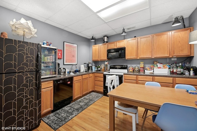 kitchen with a drop ceiling, a sink, light wood-style floors, black appliances, and dark countertops