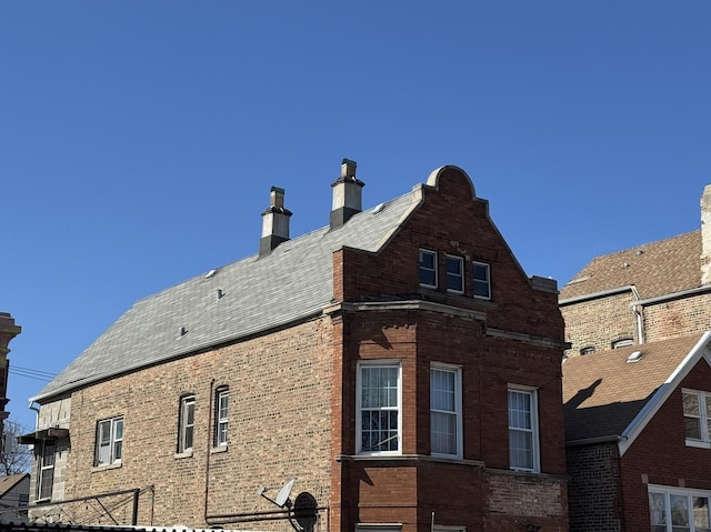 view of home's exterior featuring brick siding, a chimney, and roof with shingles